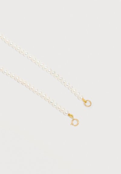 Δύο σειρές λευκών μαργαριταριών με χρυσαφένιες κούμπες πάνω σε ανοιχτό γκρι φόντο, τοποθετημένες παράλληλα και ελαφρώς κυρτές.