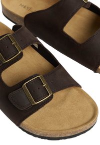 Sandalias de cuero marrón con dos hebillas ajustables, punta abierta, plantilla de corcho y suela de goma marrón texturizada. Presenta un diseño recortado en las correas.