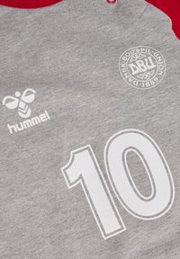 Szary T-shirt z czerwonymi rękawami raglanowymi, z białym numerem "10", logo Hummel i emblematem DBU nadrukowanymi z przodu. Miękka tekstura.