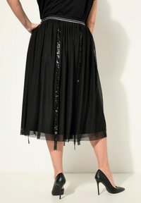 Gonna di tulle nera con dettagli in paillettes e vita arricciata, caratterizzata da una cintura argentata a contrasto. Abbinata a scarpe con tacco nere.