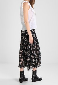 Bílý bezrukávový top s volány na ramenou, spárovaný s černou květinovou maxi sukni s růžovými květinovými vzory. Nosené s černými kotníkovými botami.