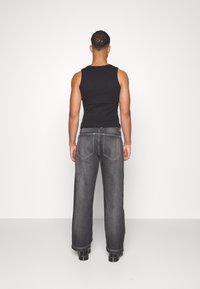 Svart linne och vida mörk denimjeans, med kontrasterande vit sömnad och rak skärning. Slät tygtextur.