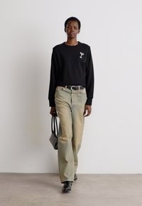 Sudadera negra con un logo de copa de cóctel; jeans de un verde claro descolorido; cinturón negro; bolso pequeño negro; botas negras de tobillo.