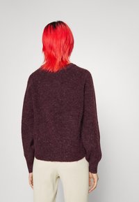 Burgundyröd stickad tröja med långa, lätt puffiga ärmar och rund halsringning, tillsammans med krämfärgade ribbade byxor. Mjuk textur, avslappnad design.