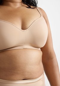 Reggiseno wireless beige in tessuto morbido, con scollatura a V e spalline regolabili. Design senza cuciture con dettagli minimi. Materiale leggero ed elastico.