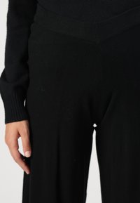 Black knit sweater and pants set featuring ribbed cuffs and waistband, soft texture, and a relaxed fit. Pants have a wide leg shape.