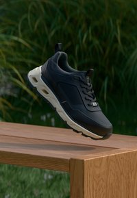 Must mustast joogid tekstuuriga pealispinnaga, valge vaheosa ja pehmendusega kaelus. Omab paelu ja silmapaistvaid külgede disainielemente.