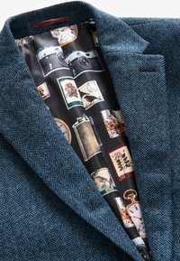 Texturierter Fischgrätblazer in Dunkelblau, mit einem gefütterten Innenfutter in Schwarz, das Vintage-Kameras, Briefmarken und botanische Illustrationen zeigt.