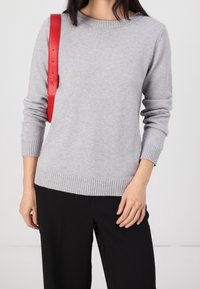 Light gray sweater in smooth knit fabric, featuring a crew neckline and ribbed cuffs. Paired with black wide-leg trousers and a red belt.