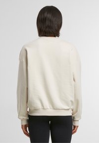 Helles beiges Sweatshirt mit lockerer Passform, überschnittenen Schultern, gerippten Bündchen und Saum. Glatte Textur und minimalistisches Design.