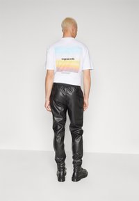 Weißes Baumwoll-T-Shirt mit einem bunten Grafikdesign auf dem Rücken, kombiniert mit figurbetonten schwarzen Lederhosen und schwarzen Stiefeln.