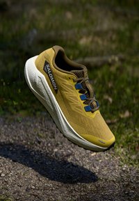 Lightweight yellow athletic shoe with a textured upper, brown accents, breathable mesh, and blue lacing system; features a white sole.