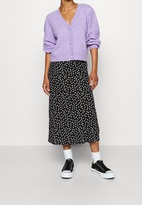 Lila stickad kardigan med V-ringning och överdimensionerade ärmar, bärs över en svart prickig midi-kjol och matchas med svarta sneakers.