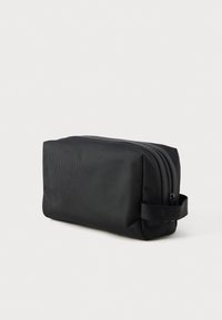 Kompakt svart rektangulær toalettveske med glidelås og sideløkke, vist mot en ensfarget lys bakgrunn.