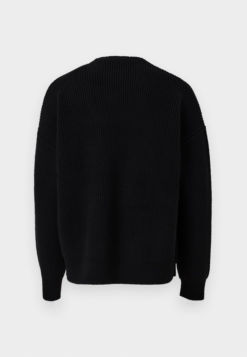 Pull en tricot noir avec une texture côtelée, encolure ronde et manches longues. Présente des fentes sur les côtés à l'ourlet pour plus de liberté de mouvement.