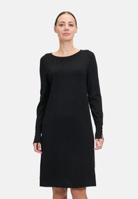 Vestito lungo nero a maniche lunghe realizzato in tessuto morbido, con scollatura a barca, decorazioni sottili e un design a taglio dritto con aperture laterali.