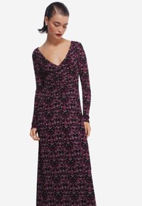 Langärmliges Kleid mit V-Ausschnitt, gefertigt aus einem dehnbaren Stoff mit floralem Muster in Dunkelrot- und Rosatönen auf schwarzem Hintergrund.