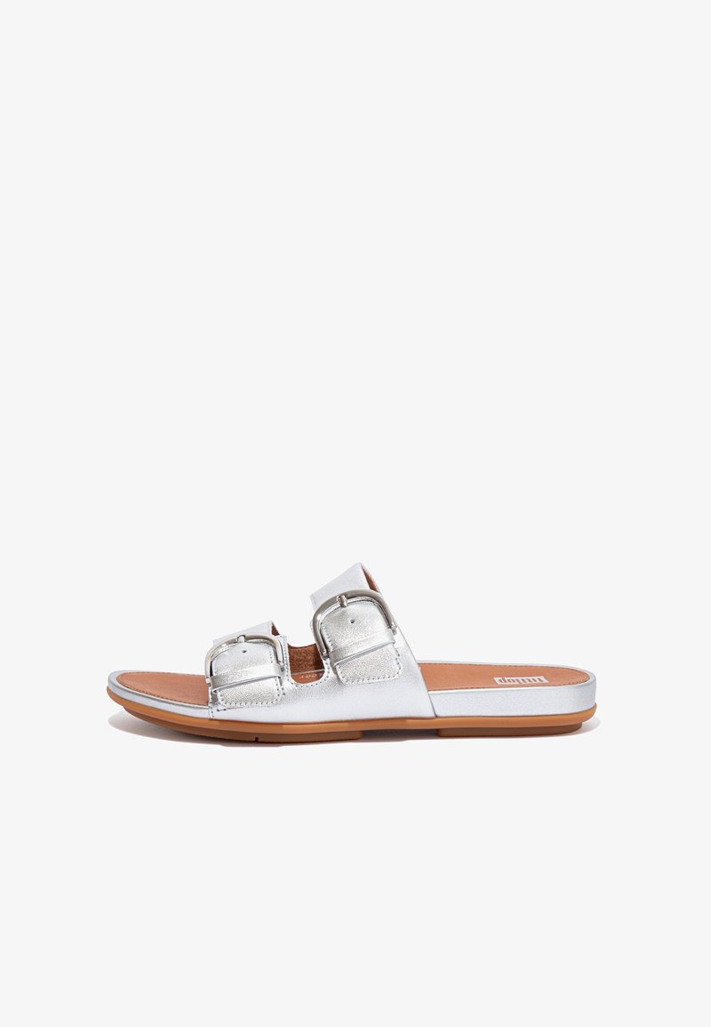 Metallic silver slide sandals with two adjustable buckles, flat tan sole, and smooth texture. Open-toe design, minimalist style.