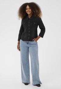Schwarzes Denim-Hemd mit Knopfleiste und zwei Brusttaschen, kombiniert mit hellblauen, weit geschnittenen Jeans. Glatte Textur und lockere Passform.