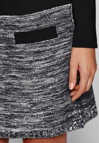 Jupe tricot noir et blanc avec une finition texturée, dotée d'une petite poche plaquée noire. L'ourlet est terminé par un bord côtelé.