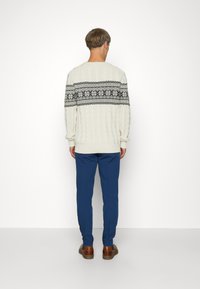 Chunky cream sweater with a black patterned yoke, paired with blue trousers. The material appears textured with visible cable knit details.