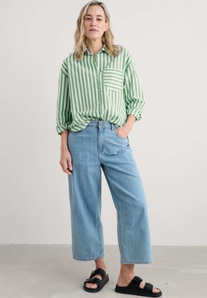 Groen en witte gestreepte button-up blouse, lichtblauwe rechte jeans en zwarte sandalen. Inclusief een borstzak op de blouse.