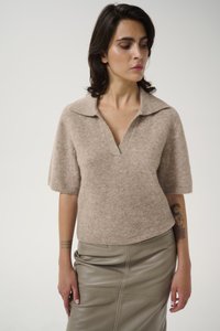 Beige strikket kortermet genser med V-hals og krage, kombinert med en glatt, tettsittende taupe skinnskjørt. Subtile tekstur- og sømdetaljer.