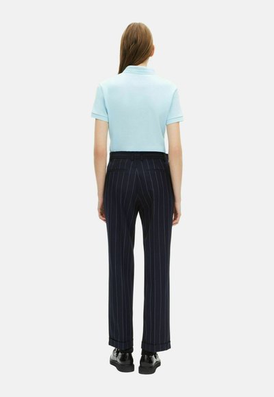 Polo shirt azzurro chiaro a maniche corte, abbinato a pantaloni scuri a righe nel colore navy. Indossato con calzature nere. Sfondo semplice.