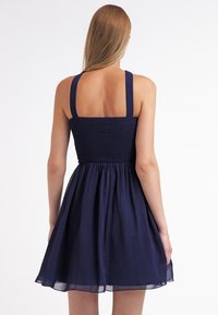 Mörkblå klänning med smockad liv och A-linjeformad kjol, med breda axelband och ett lätt, flödande tyg.