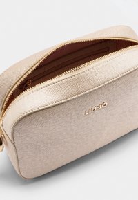 Borsa cosmetica rettangolare in materiale metallico testurizzato oro, dotata di chiusura con zip e logo del marchio sul davanti.
