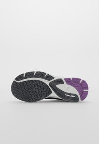 Semelle de chaussure de sport affichant un design noir et blanc, texturé avec de petits motifs triangulaires et un accent violet, étiqueté "PUMAGRIP."