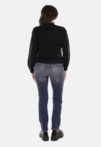 Maglione nero a maniche lunghe, abbinato a jeans attillati blu scuro. La modella indossa stivaletti neri chunky. L'immagine mostra la vista posteriore.
