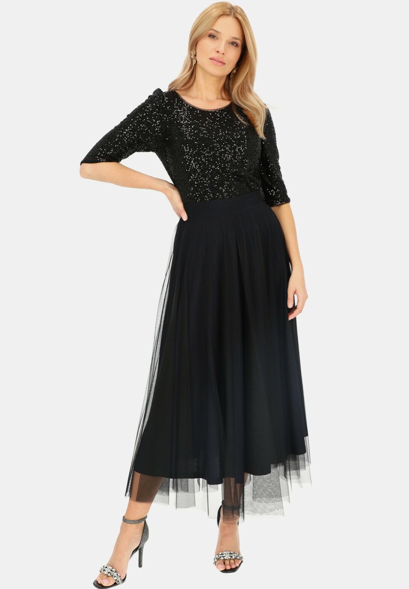 Czarny top z cekinami i rękawami o długości trzy czwarte, zestawiony z zwiewną czarną spódnicą z tiulu. Szczegóły obejmują dopasowany pas i przezroczystą nakładkę.