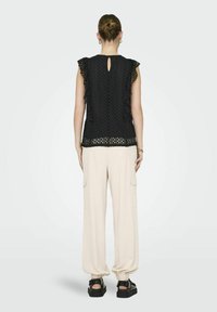 Top in pizzo nero con maniche a volant e schiena a oblò, abbinato a pantaloni beige a gamba larga con tasche e sandali neri con plateau.