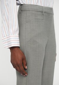 Grijze gestreepte broek van soepel materiaal, met een slim fit en zijzakken. Het geknoopte overhemd heeft zichtbaar rode en blauwe strepen.