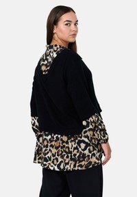 Pull court en tricot noir avec un col en V, superposé à une chemise à manches longues avec imprimé animal. Présente une coupe ample et un tissu texturé.