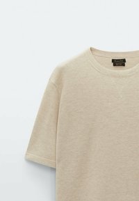 Beige cotton t-shirt featuring a textured knit pattern, short sleeves, a round neckline, and a black label near the collar.