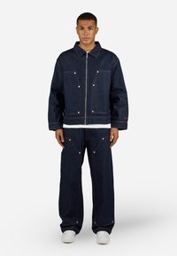 Donkerdenim jack met voorzakken en rits, gecombineerd met bijpassende losvallende broek met grote zakken en decoratieve stiksels.