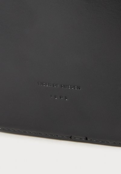 Portafoglio in pelle nera con testo in rilievo "TIGER OF SWEDEN" e "1983", texture liscia, design semplice e dettagli di cucitura discreti.