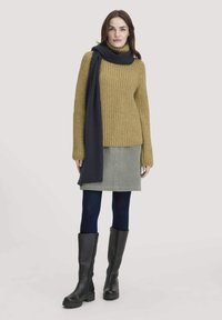 Senfgelber Strickpullover, dunkler Schal, grauer Cordrock, marineblaue Strumpfhose und schwarze kniehohe Stiefel. Lässiges Outfit mit strukturierten Elementen.