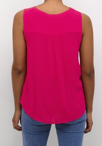 Chemise sans manches de couleur rose vif, dotée d'un col dégagé et d'un tissu doux et texturé avec des plis au dos.