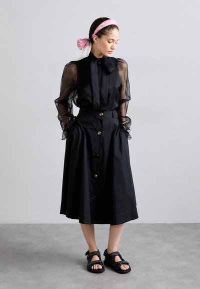 Black blouse with sheer puff sleeves and a bow at the neck, paired with a high-waisted black skirt featuring gold buttons and a flowing silhouette.
