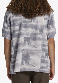 Camisa de manga corta con cuello en tejido gris claro con un patrón abstracto texturizado en gris oscuro, con un corte holgado y aberturas laterales.