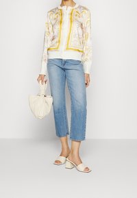 Drukowany kardigan w białym kolorze z żółtymi i różowymi wzorami, zestawiony z jasnoniebieskimi jeansami o prostym kroju oraz plisowaną torebką w kremowym kolorze. Sandały na obcasie.