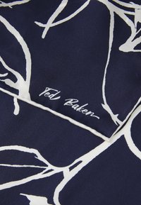 Marineblå silkescarf med et hvidt vinmønster og et "Ted Baker" logo i håndskrevet stil i kanten. Glat tekstur, elegant design.