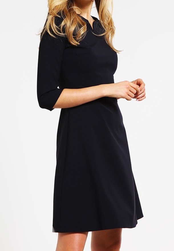 Robe marine avec un corsage ajusté et une jupe évasée. Comprend des manches trois-quarts et un col. Tissu lisse, uni, sans motifs.