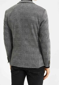 Grårutigt kavaj med distinkt rutmönster, texturerat tyg, slagkrage och knapprad på ärmen. Bärs med svarta byxor.