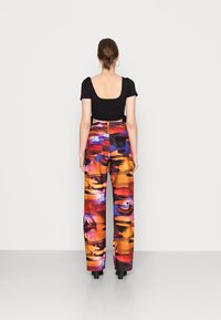 Top preto com decote redondo e mangas curtas; calças de cintura alta e pernas largas com um padrão gráfico abstrato multicolorido.