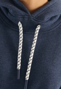 Námořnická modrá mikina s texturovaným povrchem, s bílými šňůrkami se námořnickým vzorem a kontrastními konci.