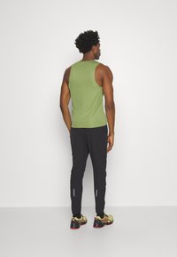 Grønt ærmeløst træningstop parret med sorte joggers. Joggers har reflekterende accenter. Modellen har lysegrønne løbesko på.